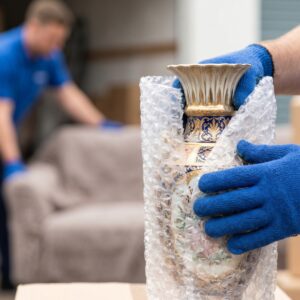 a mover’s gloved hands wrapping a delicate, antique vase with specialized, heavy-duty bubble wrap