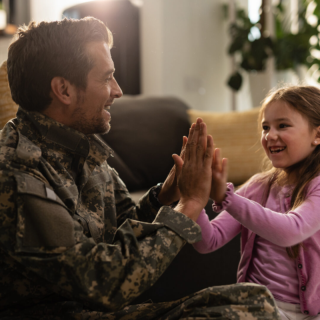 Happy little girl having fun with her military father while playing clapping hands game at home.
