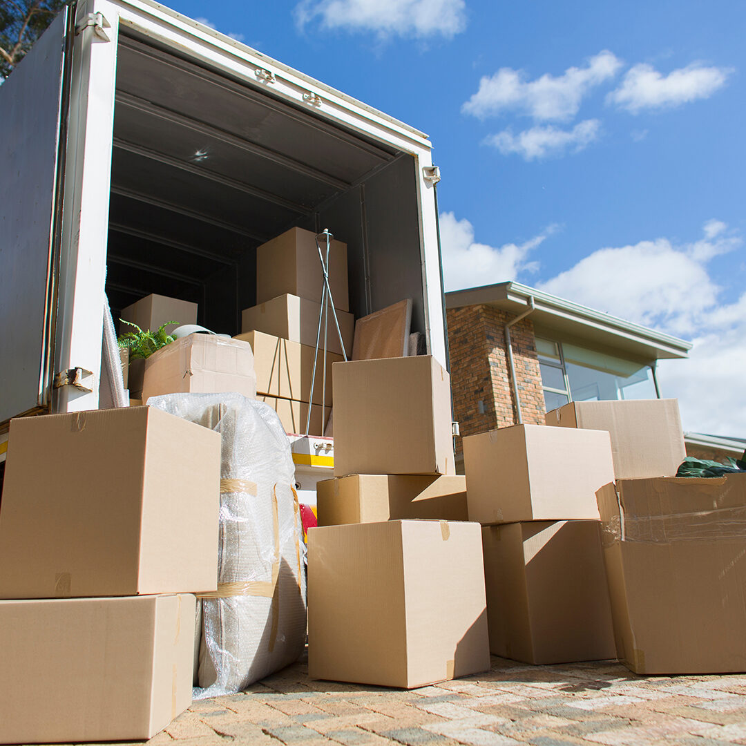 Cardboard boxes outside moving van and house in sunny driveway