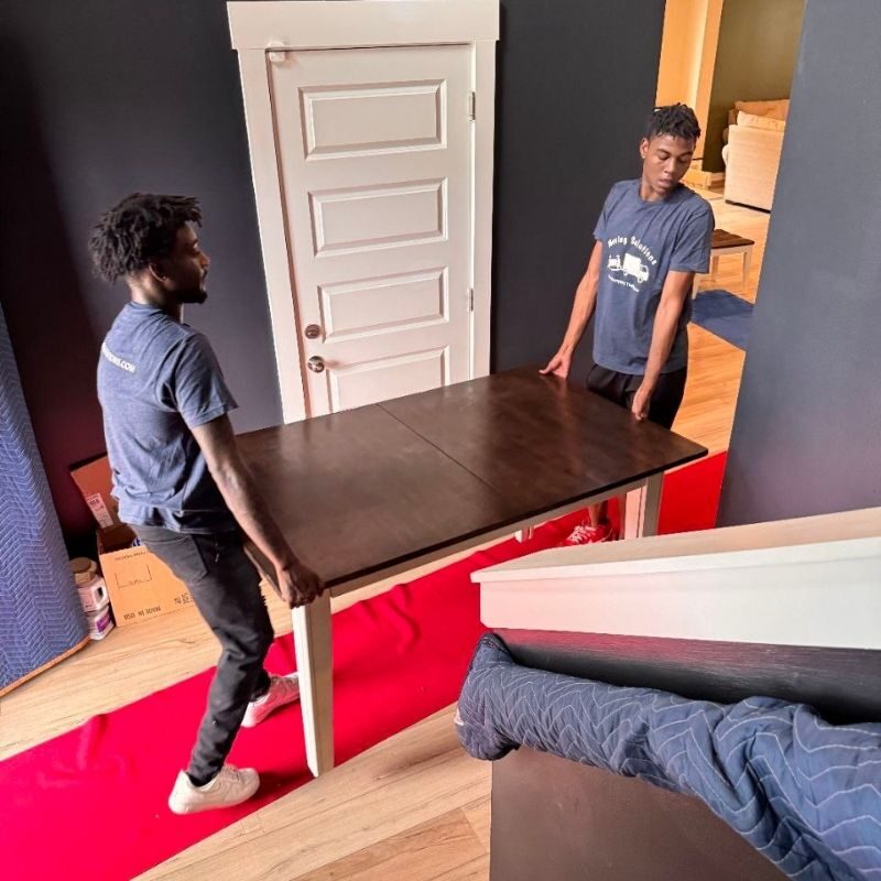 two movers bringing table into house